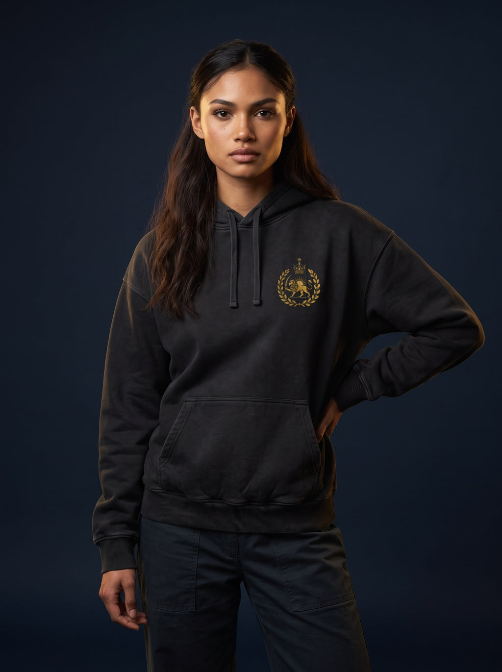 Aryamehr MIGA Hoodie schwarz, 440 g/m² Oversize – Vorderseite mit kleinem Löwe-und-Sonne-Brustmotiv, getragen von einer Frau