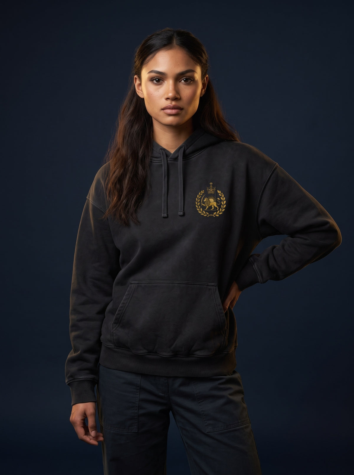 Aryamehr MIGA Hoodie schwarz, 440 g/m² Oversize – Vorderseite mit kleinem Löwe-und-Sonne-Brustmotiv, getragen von einer Frau